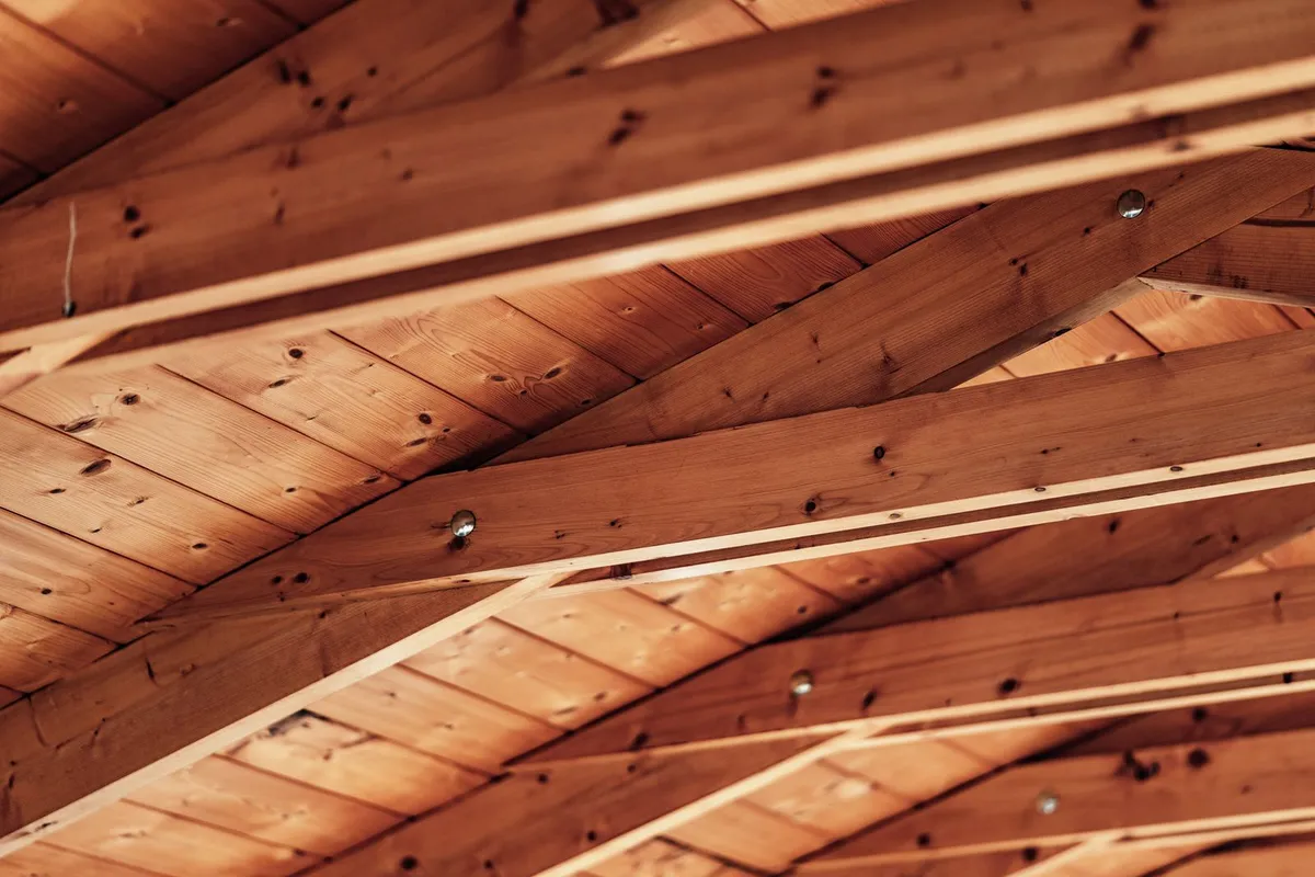 Roof beams and rafters seen from inside the attic — vent baffles keep the new insulation depth from blocking soffit airflow along this structure, which is part of the air-sealing and ventilation line in the breakdown.