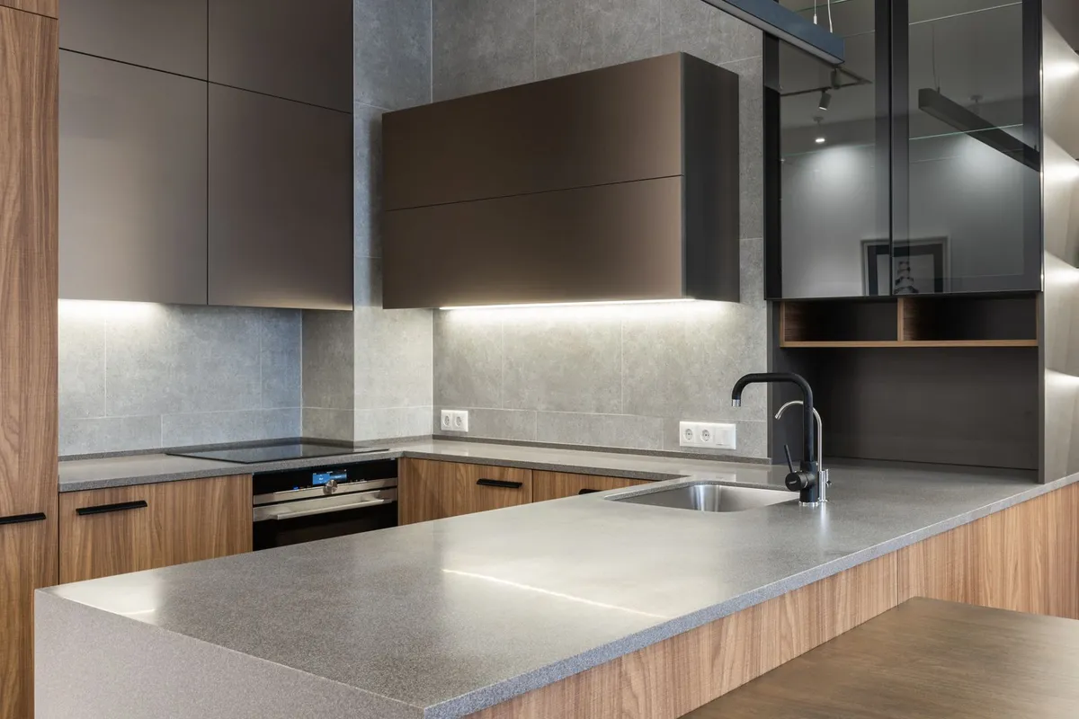 Large-format gray tile carried from the counter up the wall in a modern kitchen — tile format changes the labor maths on a backsplash: bigger tiles mean fewer pieces to set and fewer grout lines, while small mosaics and patterns are what push labor toward the top of its 35–50% share.