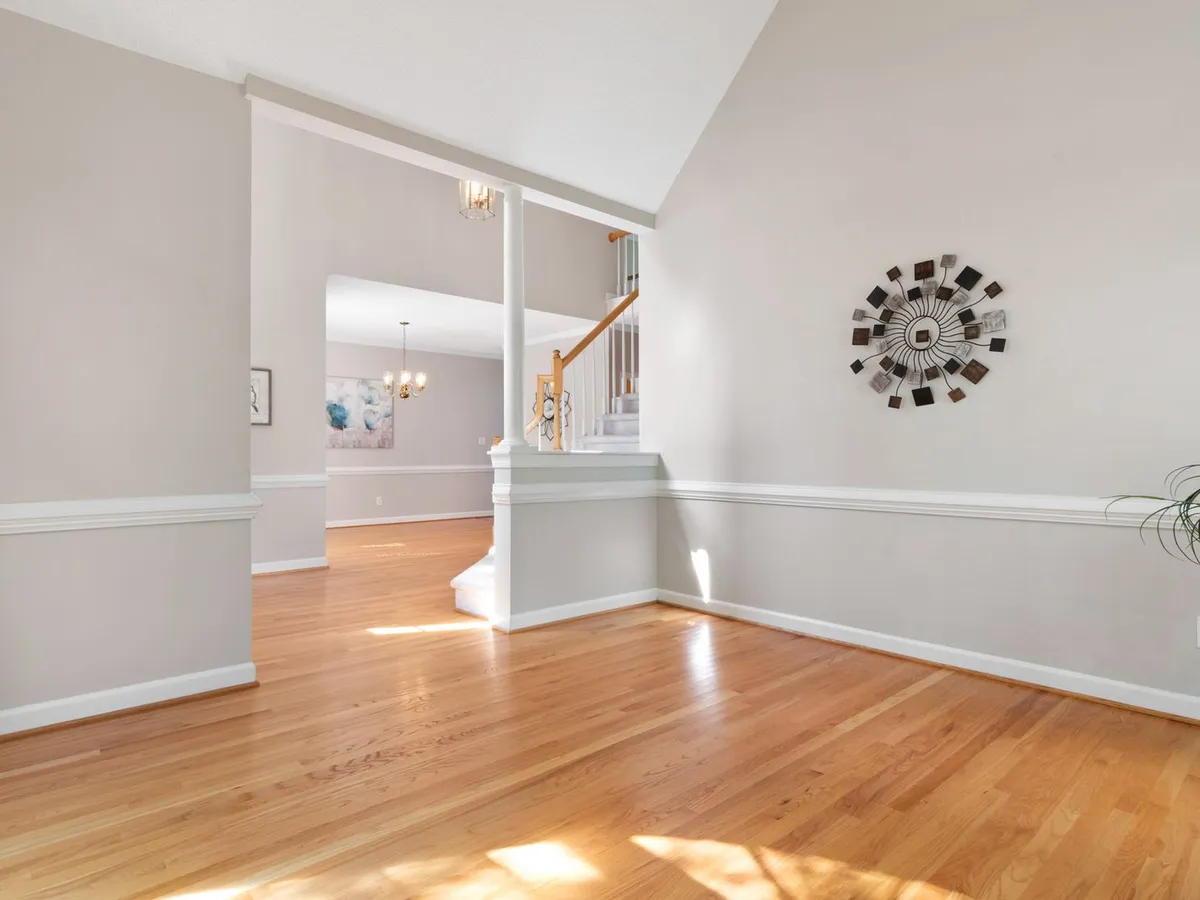 Sunlit empty room with a light honey-toned plank floor and a staircase