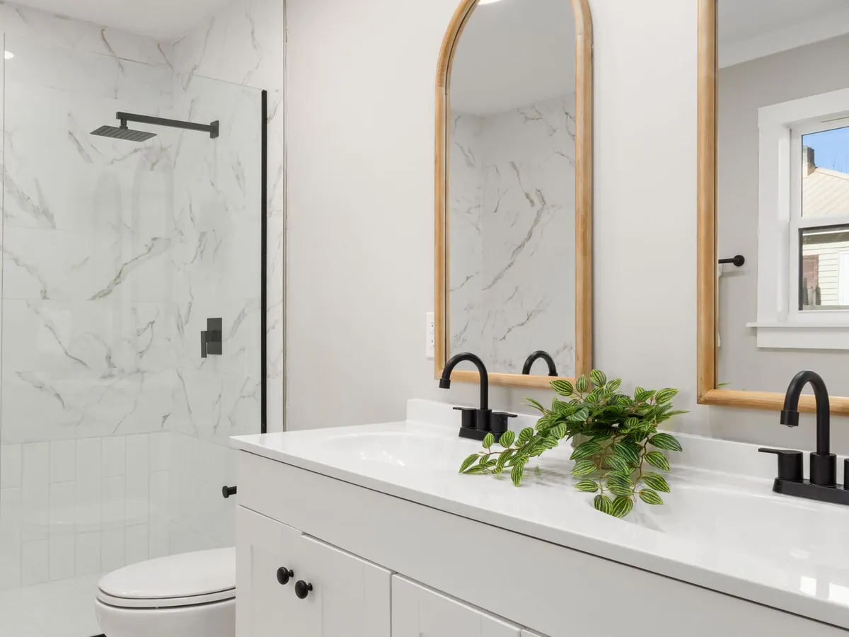 Double vanity with matte black centerset faucets and a marble-look tiled shower behind