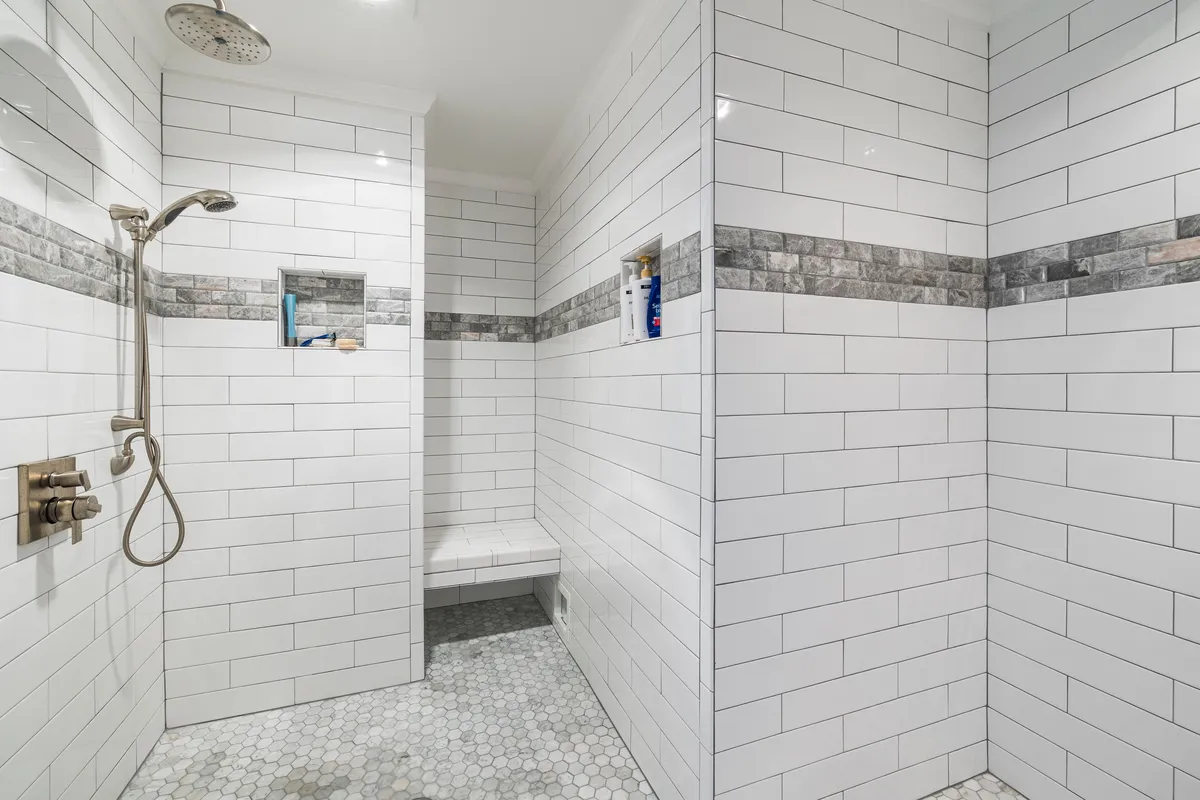 A tiled shower detail with a rainfall head and built-in bench — glass, tile grade and fixtures like these are what move a conversion from the standard tier toward the custom tier.