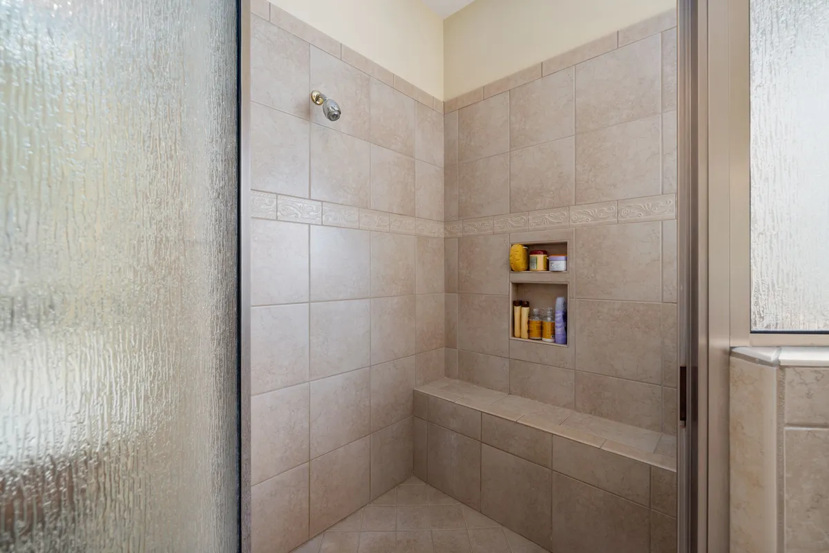 A tiled walk-in shower with a glass door, built-in bench and shelving — the pan, waterproofing and tile work behind a finish like this are the core of a standard conversion budget.