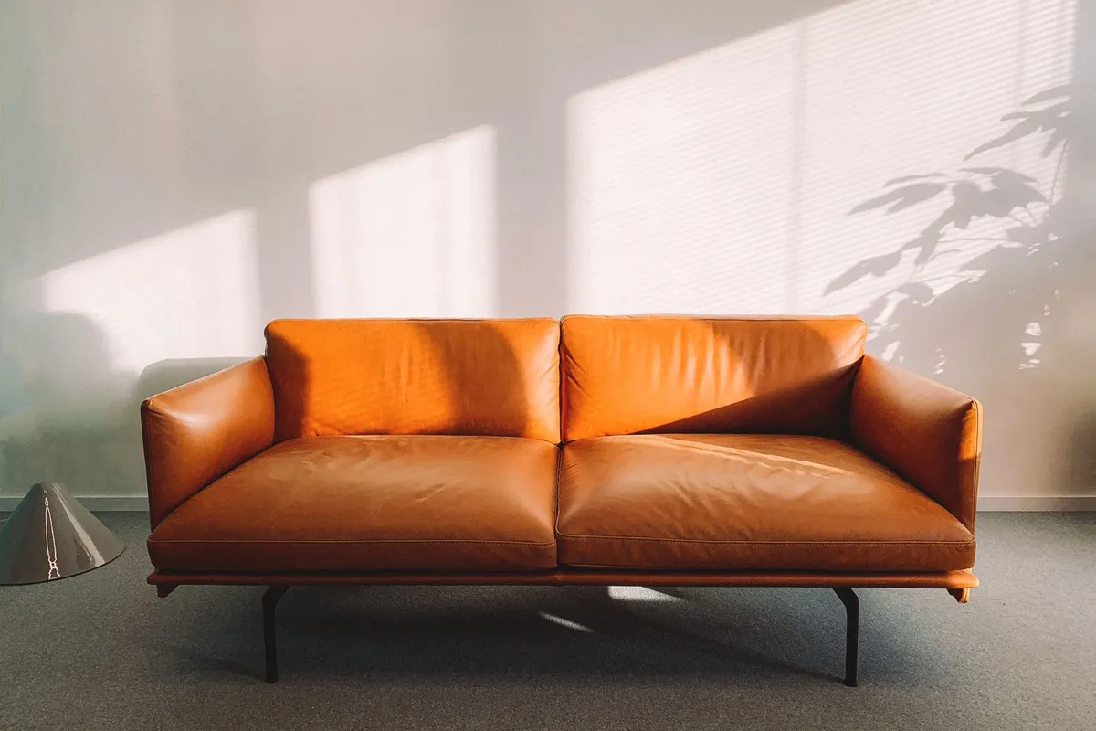 An orange leather sofa on a gray low-pile carpet — low-pile carpet like this is the living-area end of the range: it wears better under traffic and furniture than the plush bedroom piles priced at the top of the material ladder.