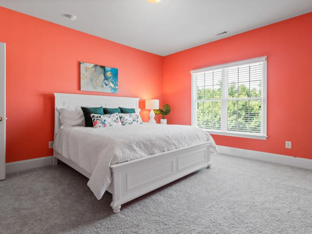 Bedroom with coral walls, a white bed and wall-to-wall light gray carpet