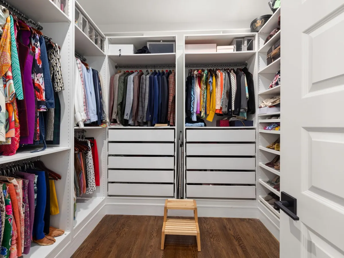 Walk-in closet with white built-in shelving, drawer banks, hanging clothes and shoe shelves