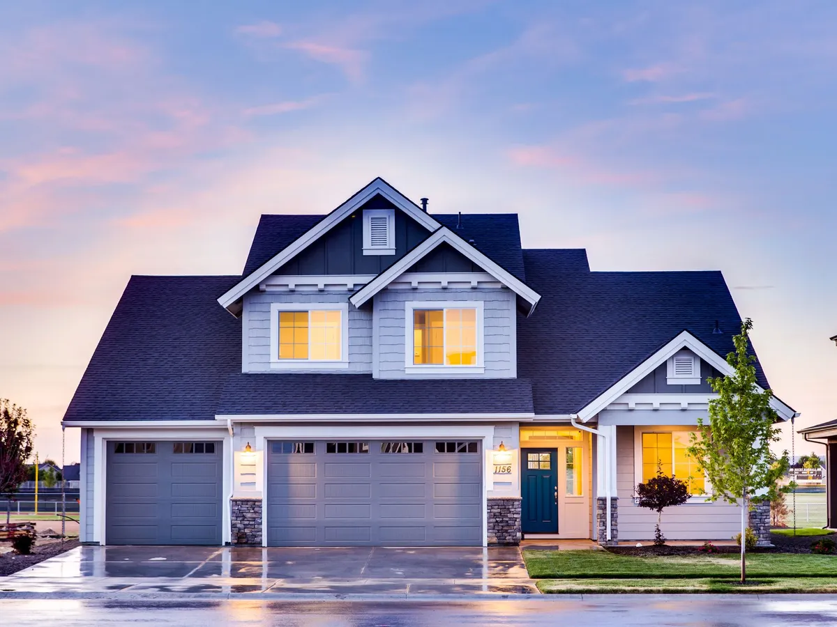 Two-story gray house at dusk with a wide concrete driveway and three garage doors
