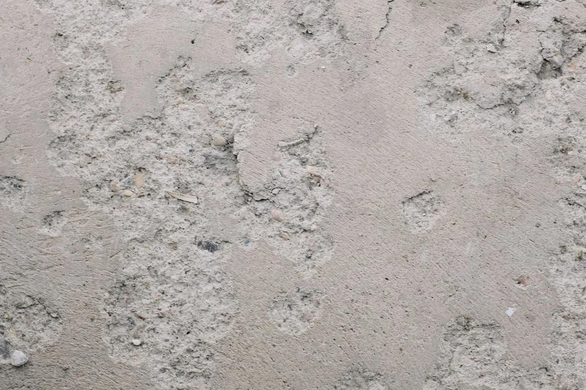 A rough, pitted concrete surface in close view — the condition of the existing slab decides the prep line: cracks, pitting and old coatings are repaired or ground out before polishing, and minor repairs run $100–$800 in HomeGuide's data.