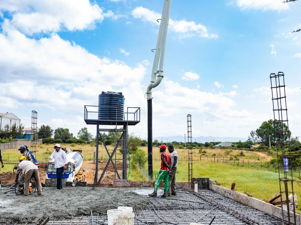 A crew placing a new concrete slab over reinforcement with a pump boom, a mixer truck behind — the pour a room needs before polishing figures apply when it has no slab