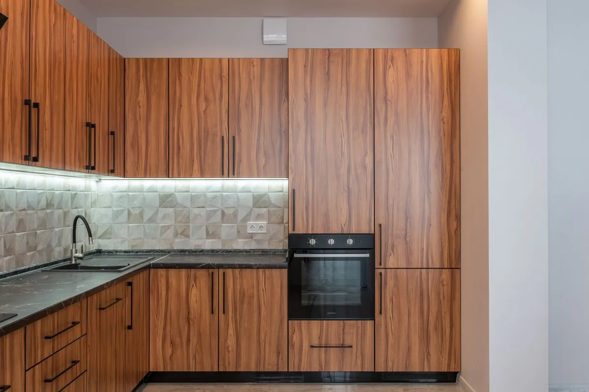 A warm walnut kitchen with its counter run and sink in close view — copper's warm tone is chosen to sit with wood cabinets like these, and the sink run is where an integrated copper sink (+$1,000–$1,500 in Angi) is priced. The pictured counter is dark stone, shown for the pairing and the scope.