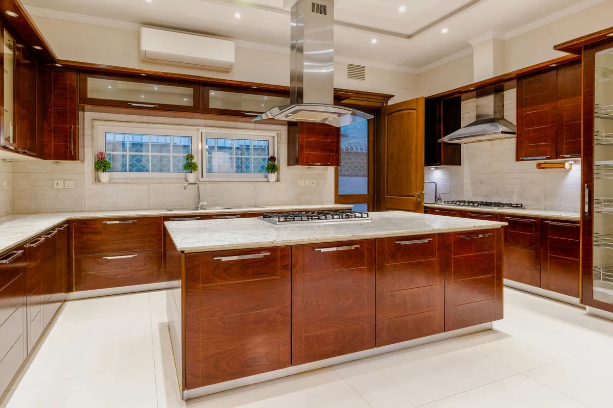 A large warm-wood kitchen with a full island and perimeter runs — at $100–$200 per sq ft installed, a full kitchen in solid copper is the splurge tier on this page, which is why most copper projects are one deliberate surface. The pictured counters are light stone; the caption describes the scope, not the material.