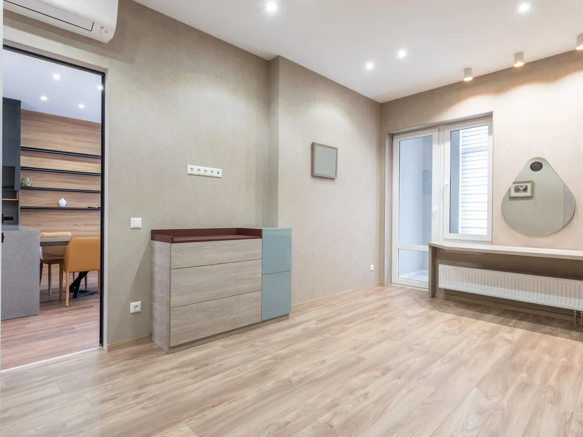 Empty sunlit room with a light wood-look plank floor and a balcony door