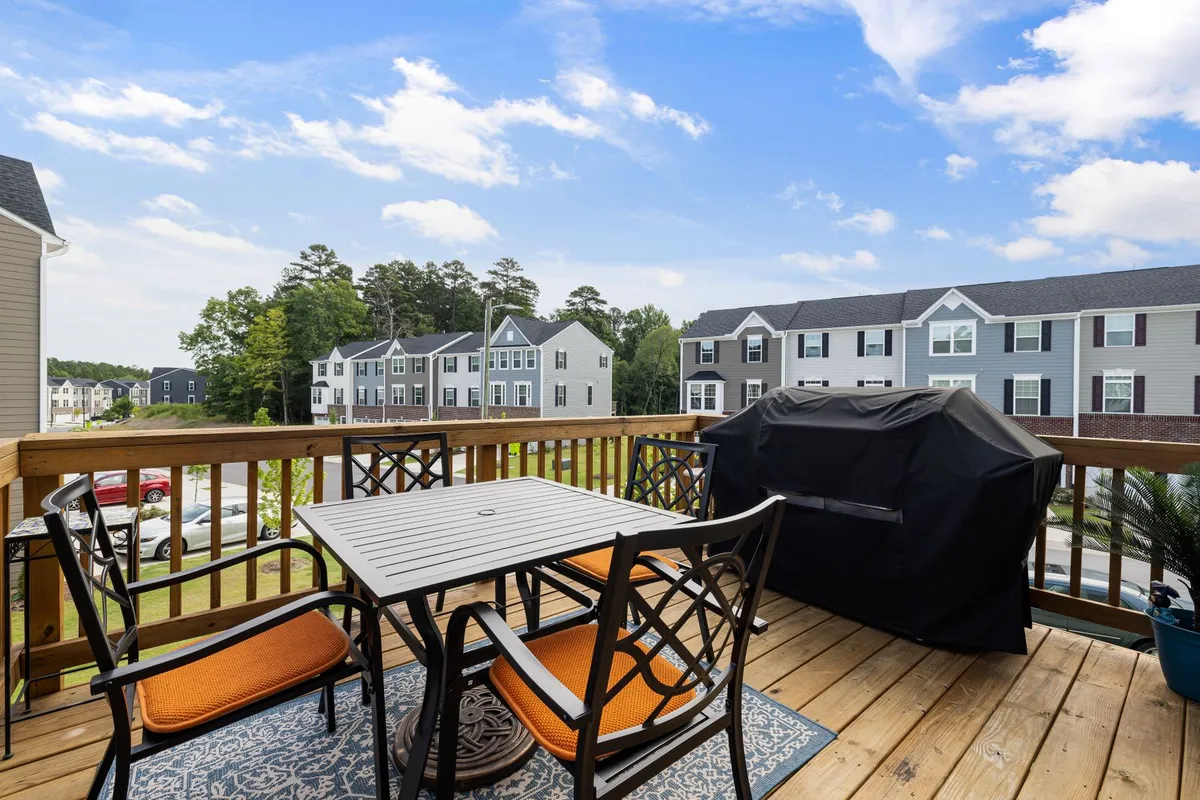 Deck boards and railing in close view, with a table, chairs and a covered grill — the finished living space a standard deck budget buys, before built-ins and premium boards push it higher.