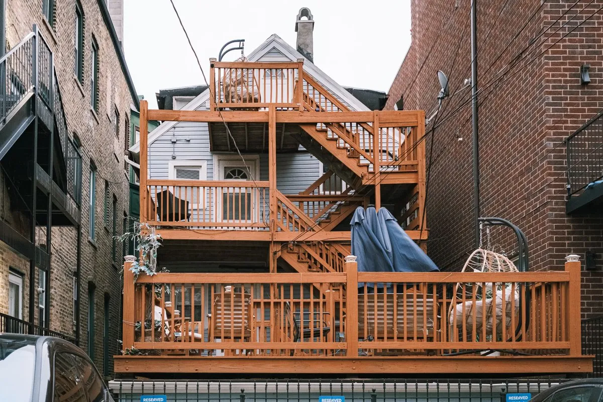 A multi-level wooden deck with stairs and railings between two houses — levels, stairs and code railing are the features that move a deck from the standard tier toward the top of the range.
