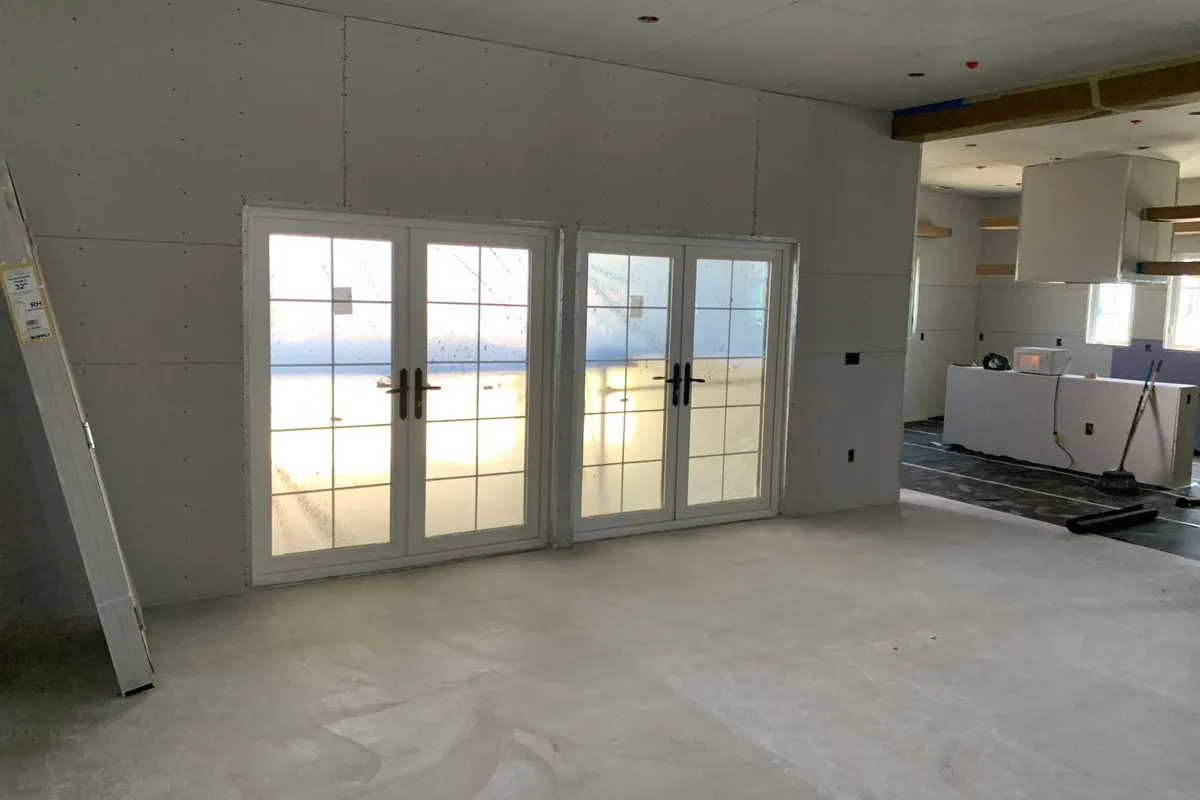 A hung drywall wall with French doors fitted and a spare panel leaning ready — board material is only 15–25% of the budget; the finish level applied over panels like these is what the rest buys.