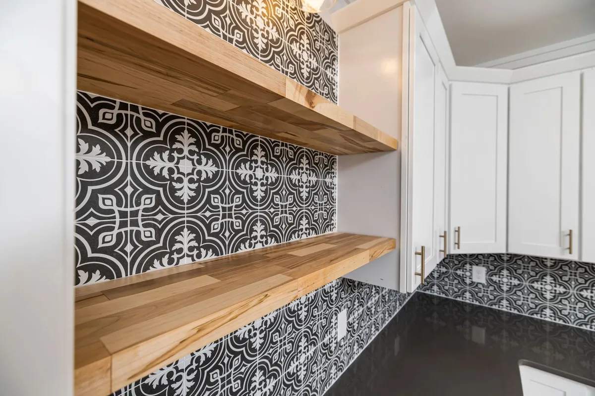 A glossy black counter run reflecting a patterned tile splashback — a solid-colour glossy pour is epoxy's simplest finish, and its mirror surface is why prep and repairs ($225–$550 in Angi) are priced before the pour, not after. The pictured counter is not certified as epoxy.