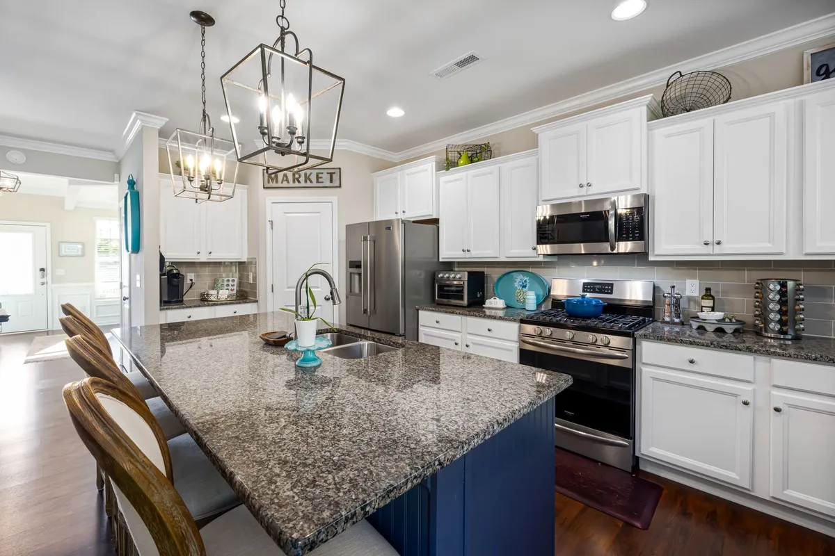 A polished speckled island counter in the foreground of a white kitchen — a stone-look finish like this is the hand-worked end of epoxy work, and the veining labour is what pushes a pour toward the top of the $50–$150 per sq ft band. The pictured counter is not certified as epoxy.