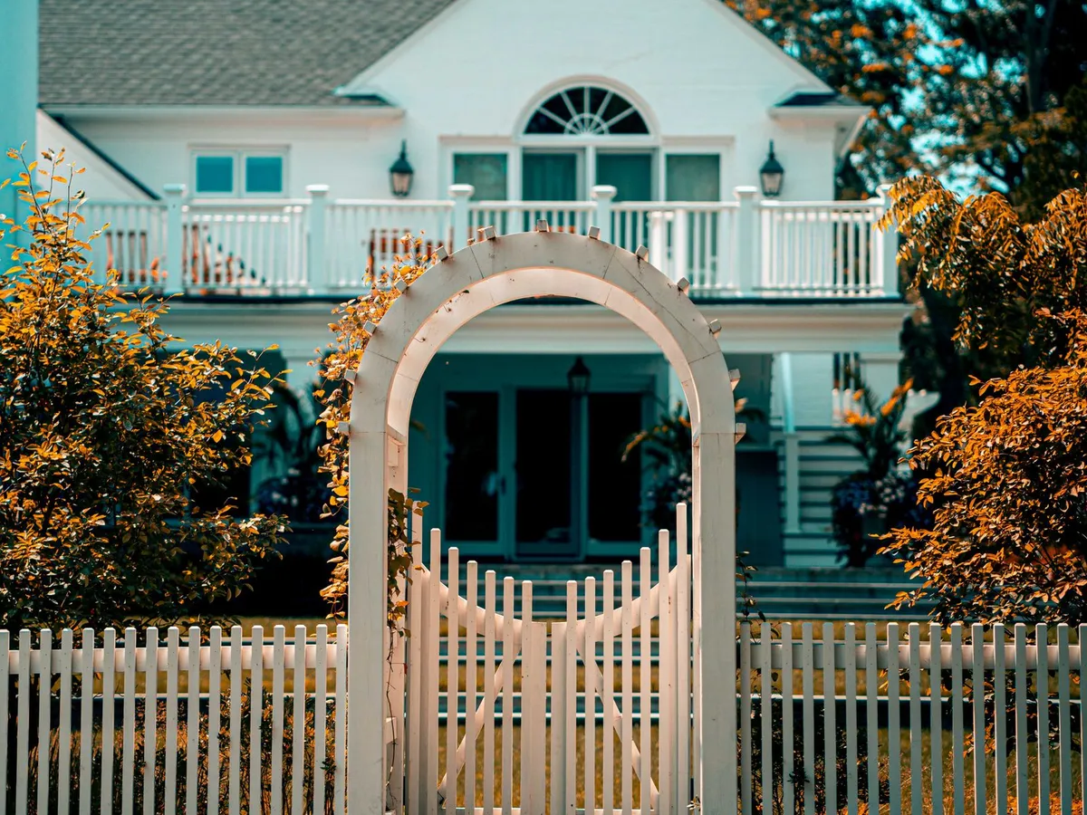 White picket fence with an arched gate in front of a two-story house