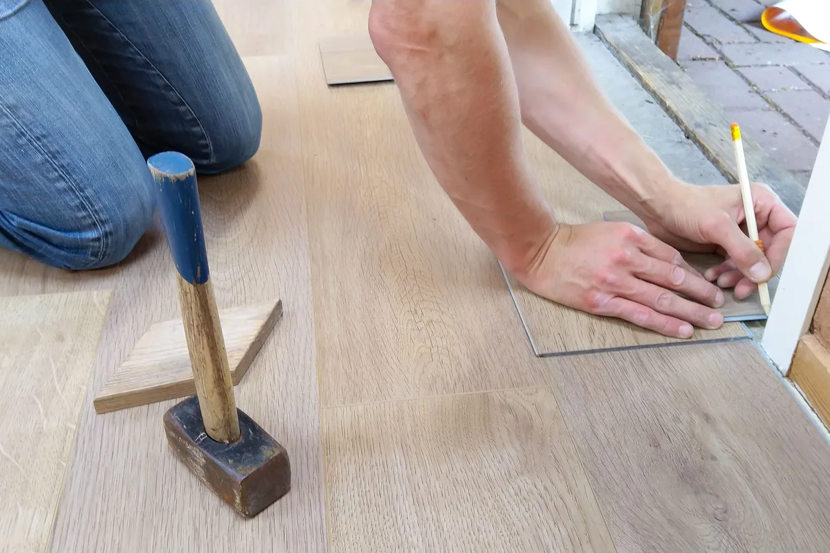 Measuring and marking wood planks during a floor installation — careful layout and cuts are the labor half of a flooring budget, next to the material itself.