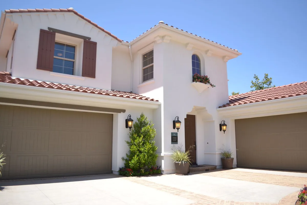 A stucco house with two tan panel garage doors — door count, size and panel style are set before material and insulation move the price.