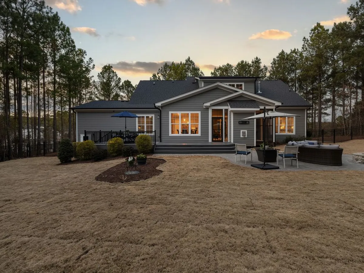 Rear of a house at dusk with the lights on and a wide yard beside it