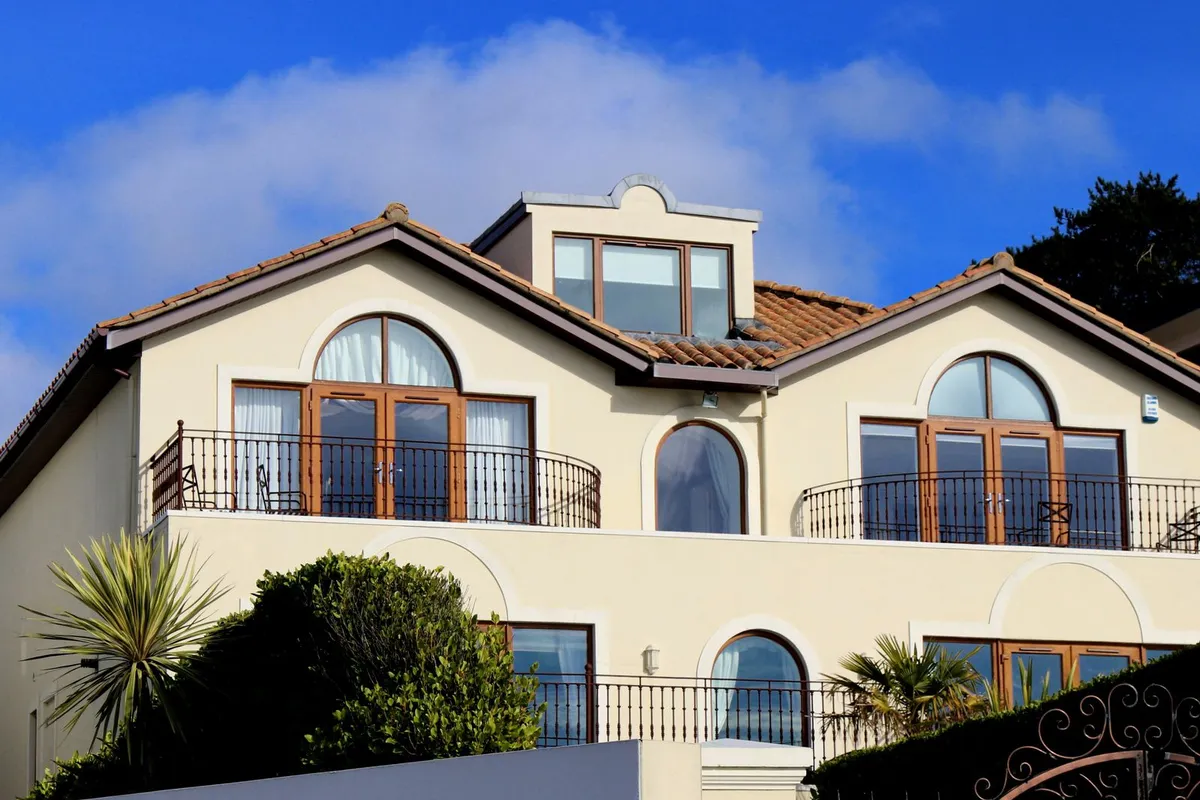 A large house with a tiled roof and a gutter run visible along the central eave — the gutter is priced by the linear foot of eave it serves, whatever the roof above it is made of.