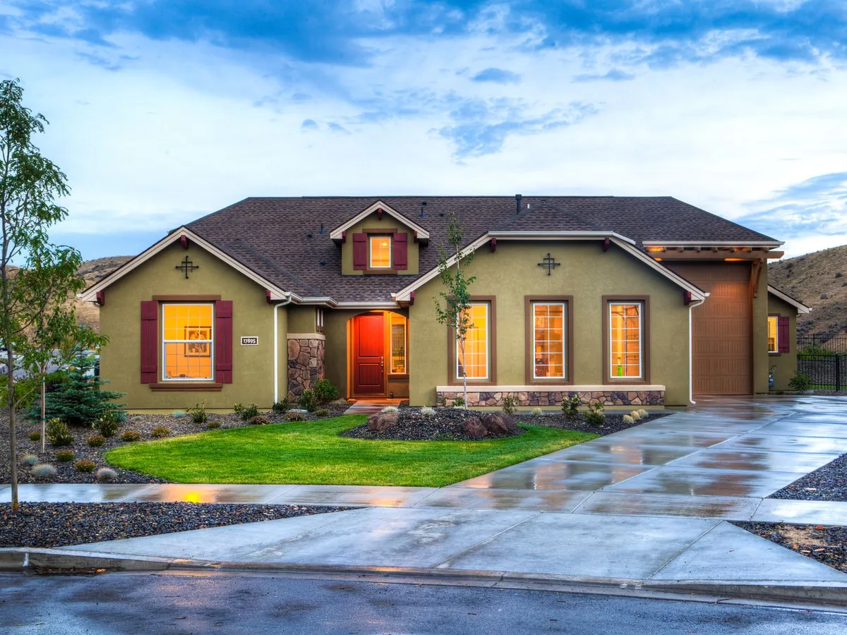 Single-story house at dusk with a shingle roof, gutters and downspouts, and a wet driveway after rain
