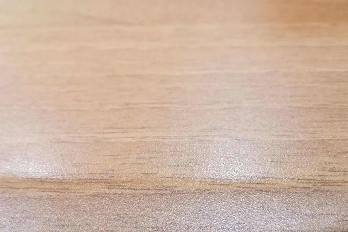 A light wood floor surface in close view, showing grain and sheen — the finish coats are the visible result of a refinish, priced at $1–$2 per sq ft as a stage in Angi, on top of sanding and staining.