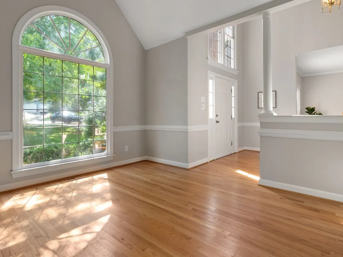 Sunlit living space with a newly installed light hardwood floor and a large arched window