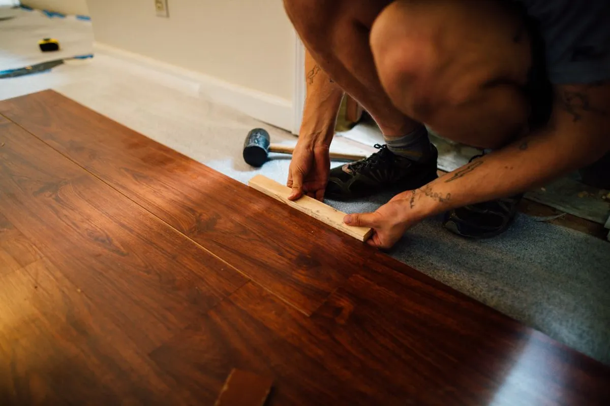 An installer fitting dark hardwood planks with a tapping block — installation labor is 30–40% of a hardwood budget, and nail-down solid boards are the slowest version of the job.