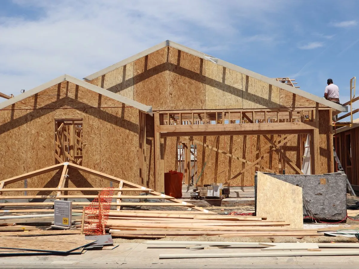 Wood-framed house under construction with OSB sheathing and roof trusses on site