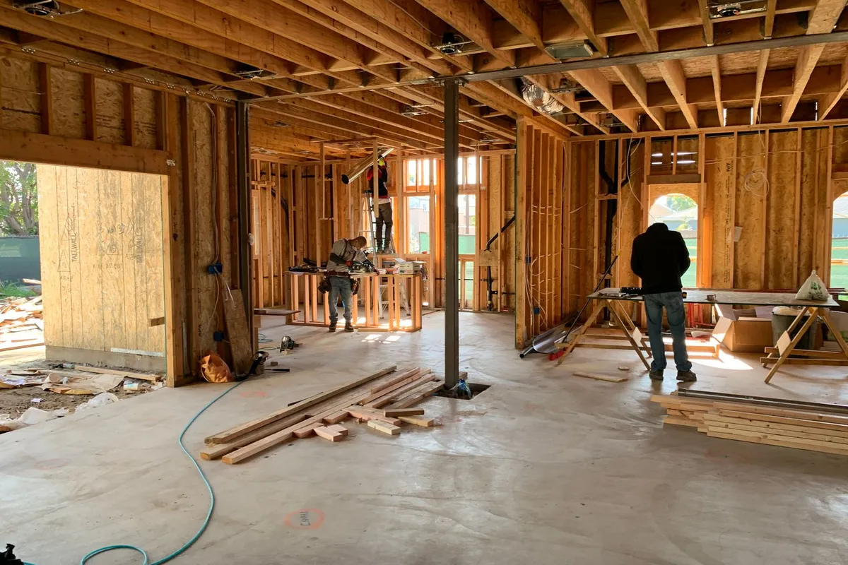 Workers inside the wood framing of a new addition, joists and studs exposed — the structure (foundation, framing, roof and exterior) is the largest share of an addition budget.
