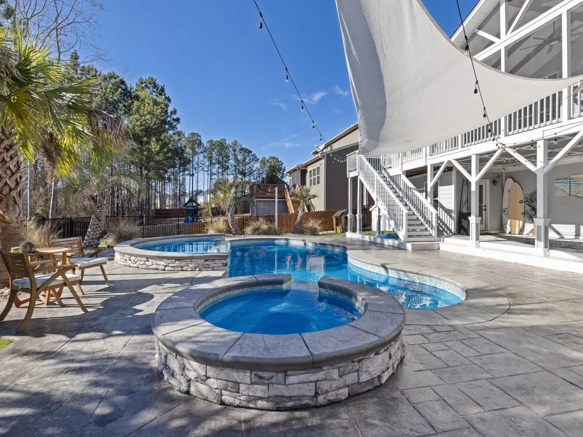 Raised round stone-clad spa beside a backyard pool on a stamped-concrete patio