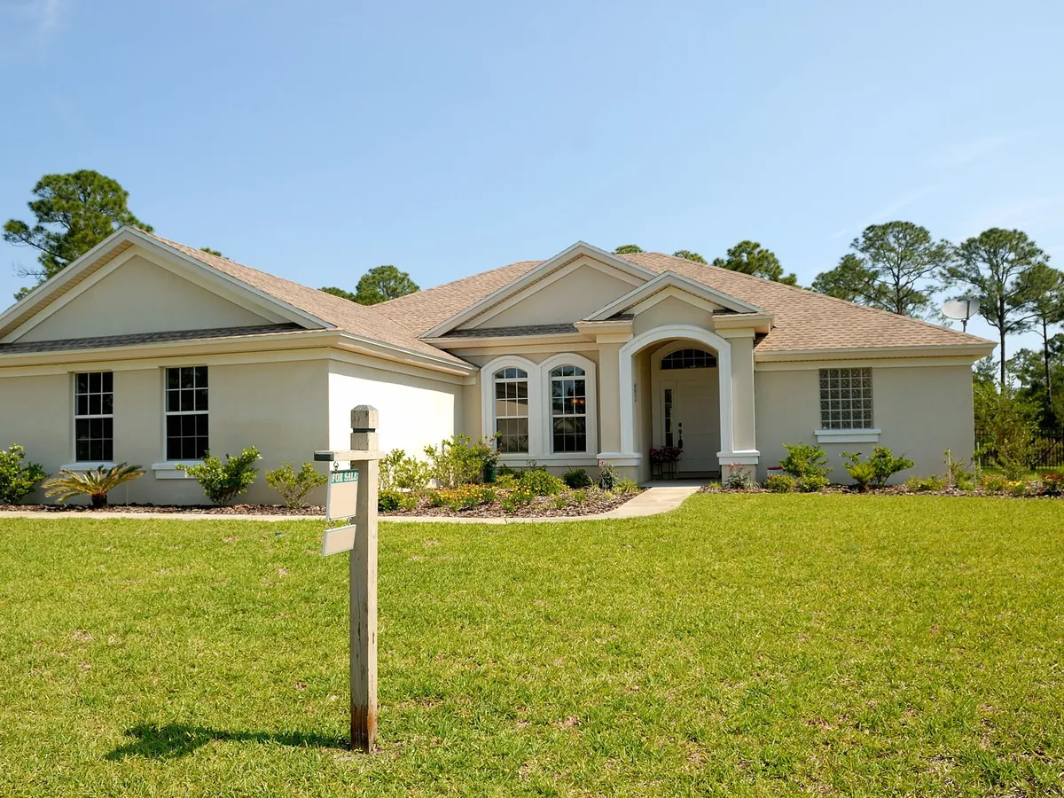 Single-story beige stucco house with a freshly painted exterior, neat lawn and concrete walkway