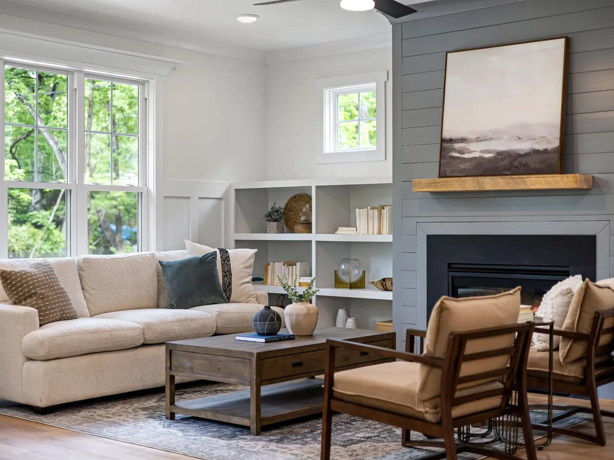 Bright finished living room with a cream sofa, painted shiplap fireplace wall and large windows