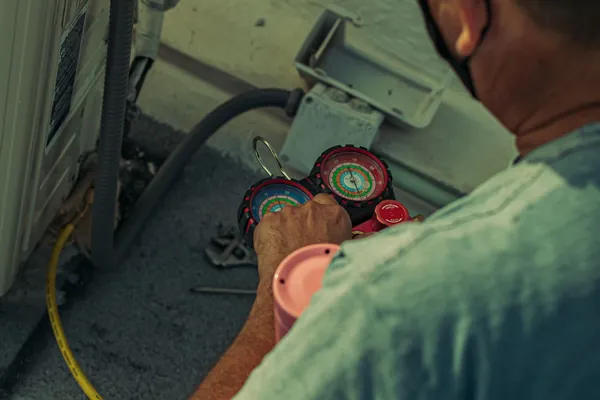 Technician servicing an outdoor air conditioning unit with manifold gauges and hand tools