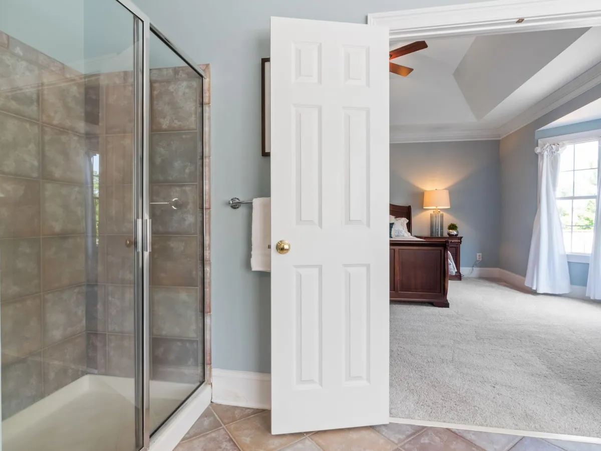 Open white six-panel interior door between a tiled bathroom and a carpeted bedroom