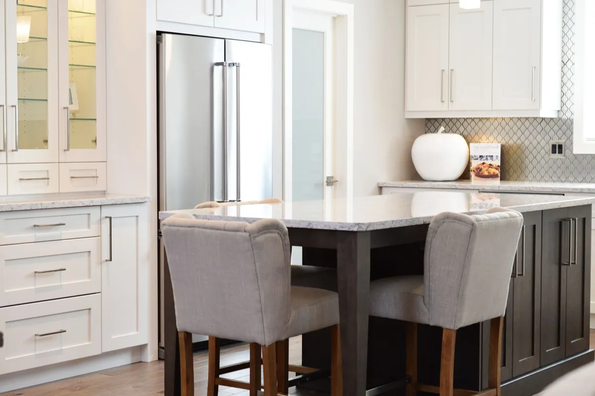 White cabinets with glass-front uppers and a dark island — glass fronts, specialty storage and a contrasting island are the upgrades that move a kitchen from the stock tier toward semi-custom.