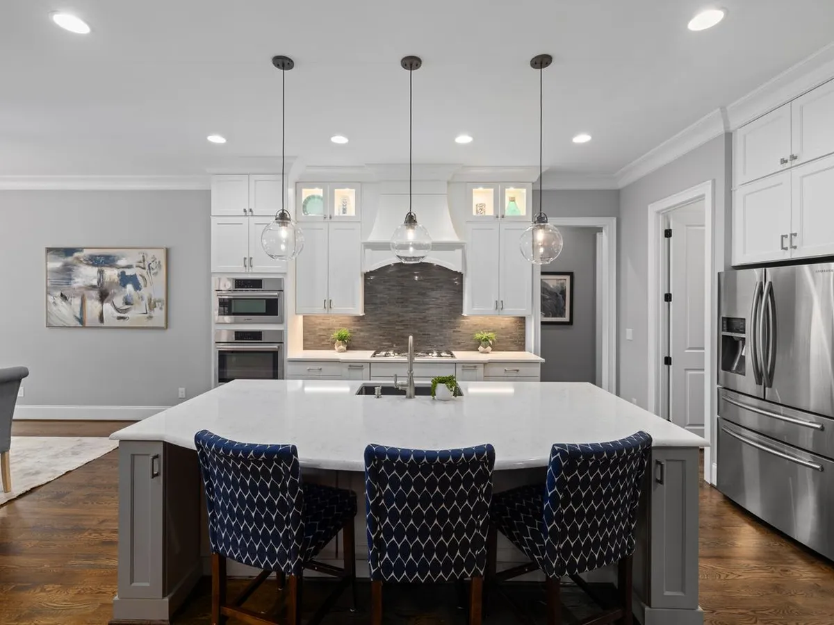 White kitchen with a large island with a sink and seating for three, pendant lights above