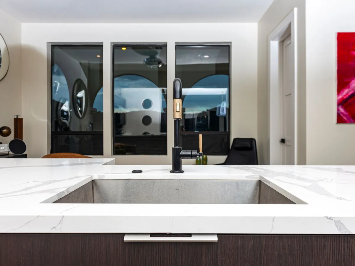 Undermount kitchen sink set into a white stone island counter with a black pull-down faucet