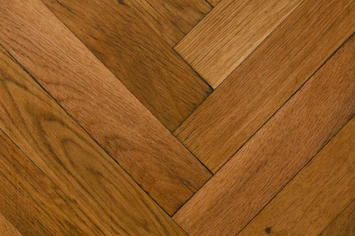 A herringbone-pattern floor in close view — patterned lays are the premium end of laminate work: more cuts, more waste and slower fitting than the straight lay every per-square-foot average assumes.