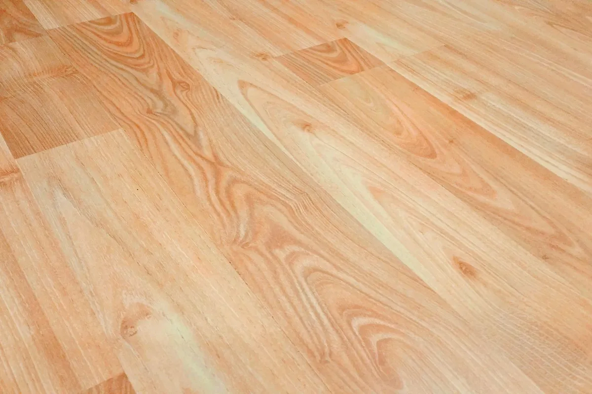 Light wood-look laminate planks in close view — the printed image layer is the product: material runs 40–55% of a laminate budget, and thickness and wear rating are what separate the boards that look like this for a decade from the ones that do not.