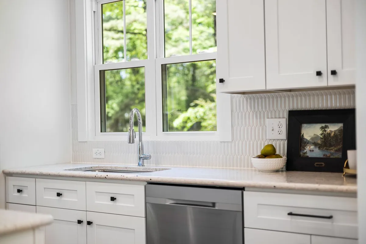 A white kitchen sink run with a light stone counter and a tiled backsplash — a kitchen run like this is priced by the same slab-plus-labor maths as the vanity above, with each sink and cooktop cutout counted in fabrication.
