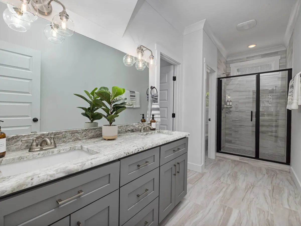 Bathroom with a double vanity topped with white veined stone countertops and a glass-enclosed shower