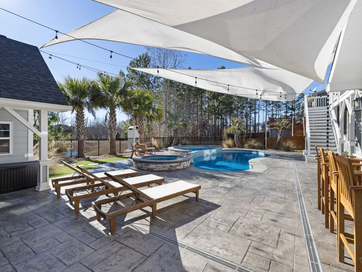 Stone-look paver patio around a pool with shade sails and loungers
