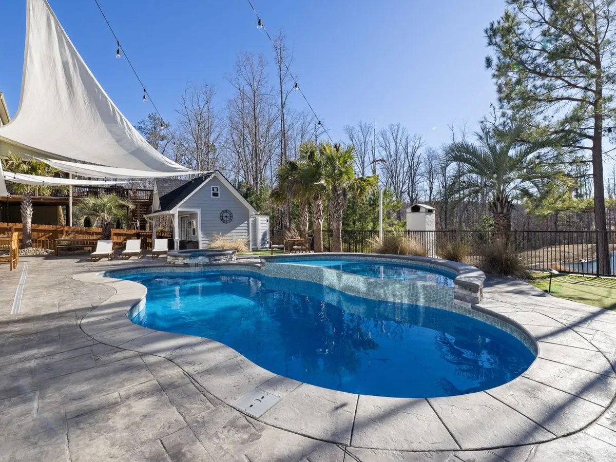 Pool patio shaded by large white shade sails over a paved patio