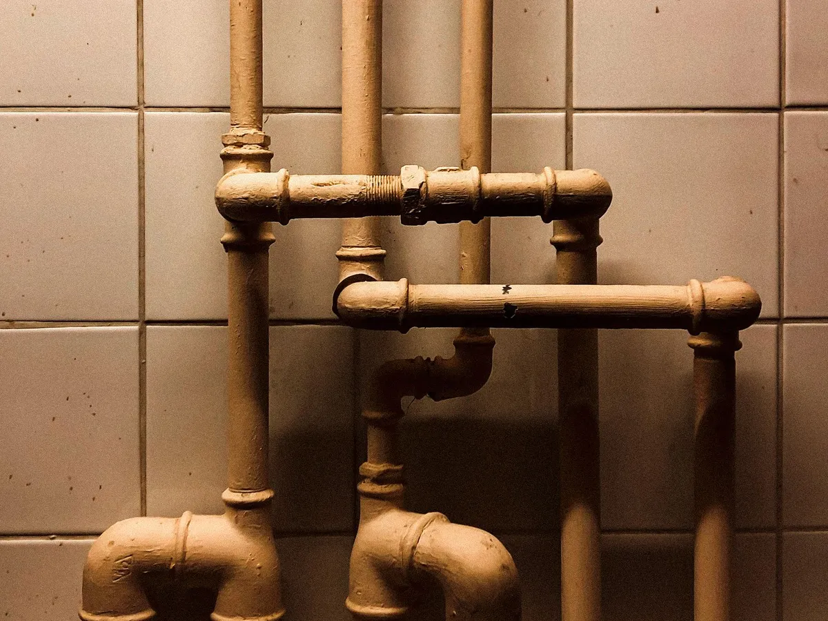 Aged painted metal supply pipes and traps against a tiled wall — the end-of-life piping a whole-house repipe replaces
