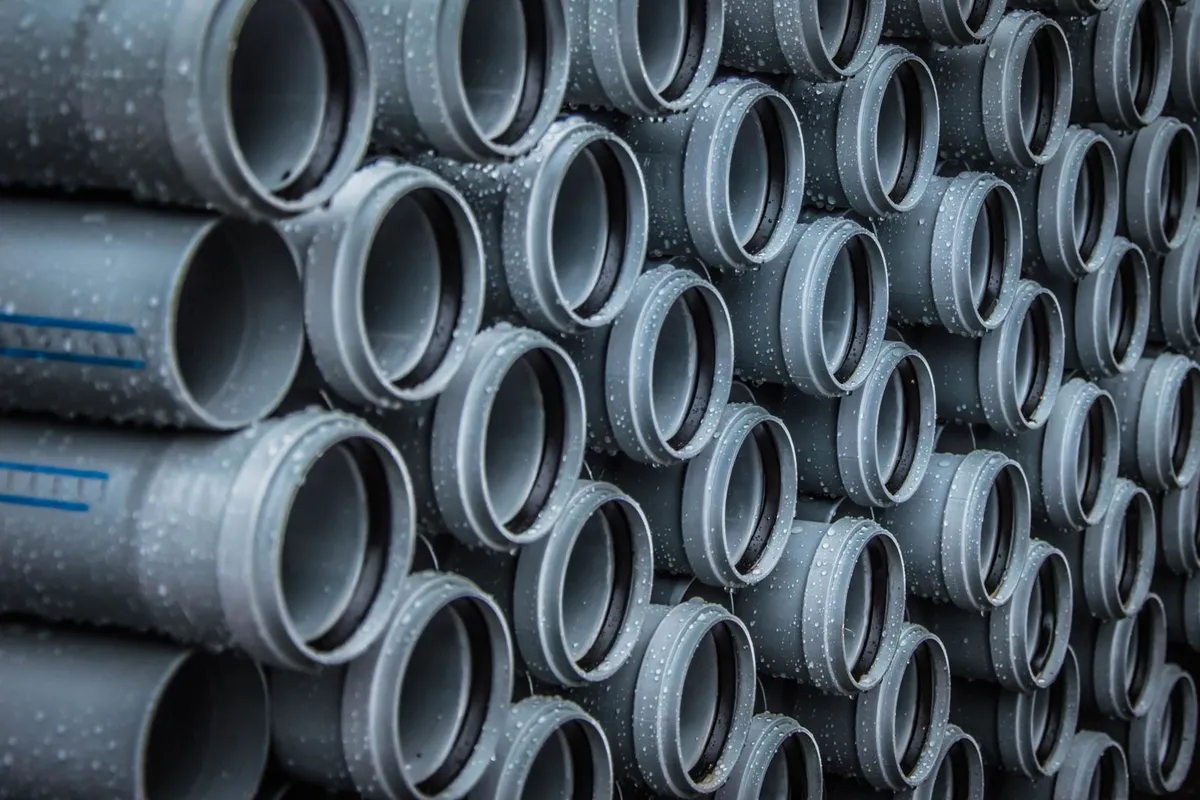 New gray PVC pipe stacked ready for installation — the pipe itself is only 15–25% of a repipe budget; routing it through a finished house is the labor that makes up most of the bill.