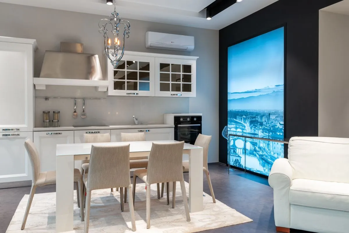 The same white kitchen from the dining side, white counter run behind the table — edges are the porcelain decision: a square edge is usually included, a built mitered edge is priced per linear foot.