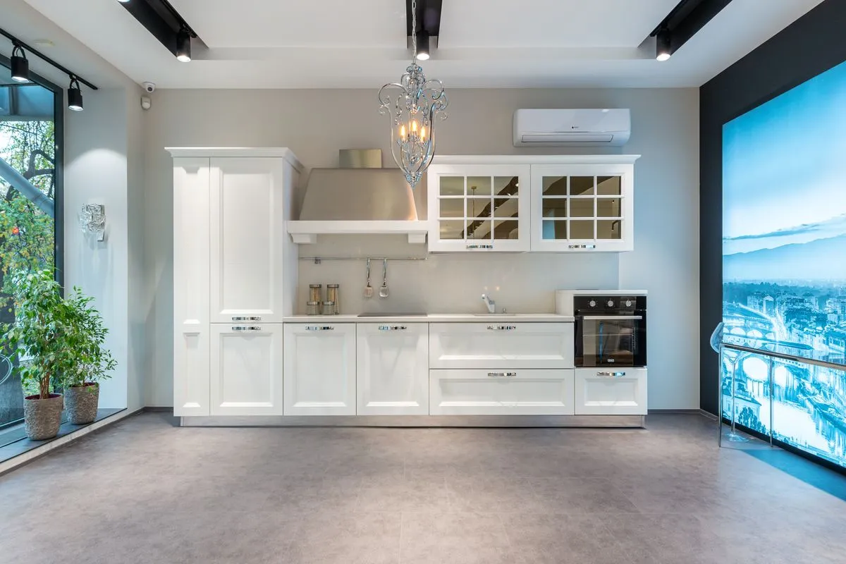 A white kitchen run seen full-width with a thin white counter — fabrication and installation are 40–55% of a porcelain budget, because a thin slab is brittle until the moment it is set.