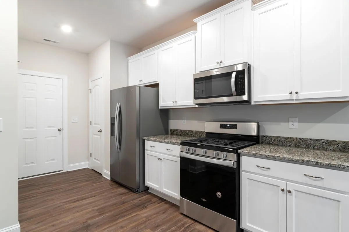 A white kitchen with speckled counters either side of a stainless range — slab material and fabrication are 55–70% of a recycled-glass budget, and the speckle pattern is the glass showing through the binder.